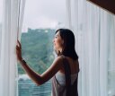 Beautiful young Asian woman opening curtains and looking out to the beautiful scenics through window in the morning. A brand new day with hope and possibilities
