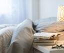 A bed with a lamp, books and glasses on a bedside table. 2021 was a great year for sleep research.