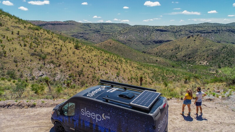 Friends stand outside their camper van looking at scenery.