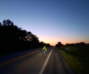 A cyclist in a florescent windbreaker and helmet dashes across an empty road with the sun fading on the horizon. Race Across America, or RAAM athletes train to get little to no sleep during the 3,000 mile race.