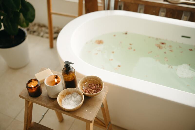 Bath tub with candles, bath salts, and dried flowers on a side table.