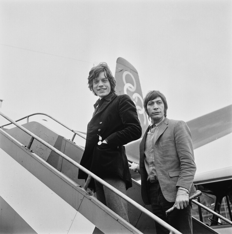 Mick Jagger and Charlie Watts smiling at a camera on airplane atairs.