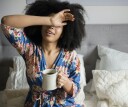 Woman sitting in bed, drinking a cup of coffee to help her wake up in the morning
