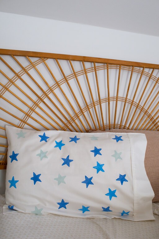 A potato stamped pillowcase with a star design rests against a headboard. this is a great DIY craft project to do with kids.