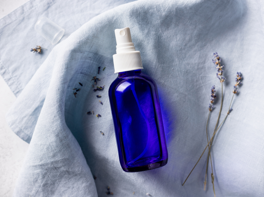 A blue spray bottle on a light blue sheet with lavender flowers scattered around it.