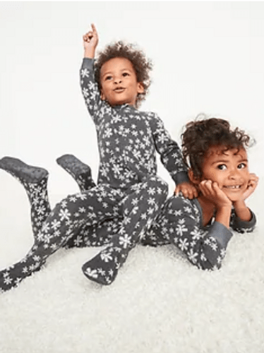 A young boy sitting on a slightly older girl's back in their matching family Christmas pajamas.