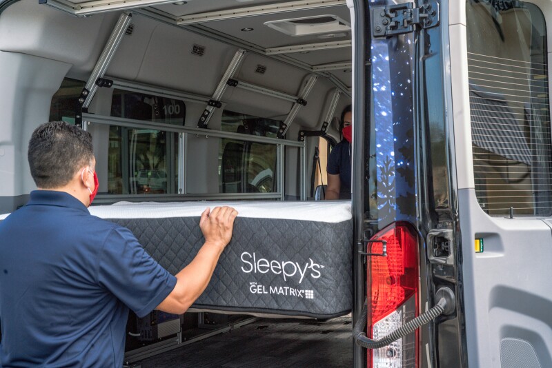 Mattress Firm Sleep Experts load a Sleepy's mattress into a camper van.