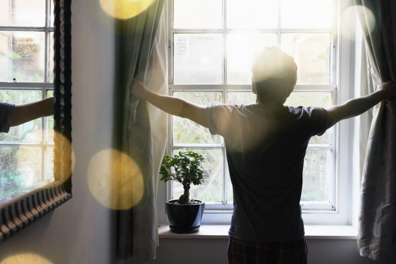 Man opening curtains to let light in