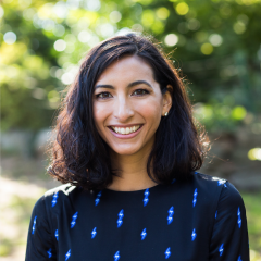 Headshot of writer Deanna Pai. She's standing outside and wearing a navy blue shirt with lightening bolts on it.