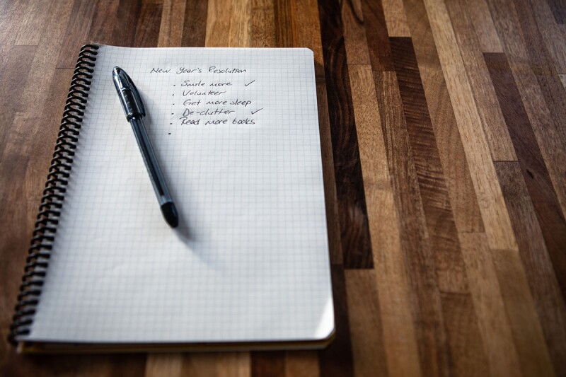 A notebook with sits on a table, with a pen resting on the page. There is a bulleted list on the paper with New Year's resolutions, including one to get better sleep in 2022. 