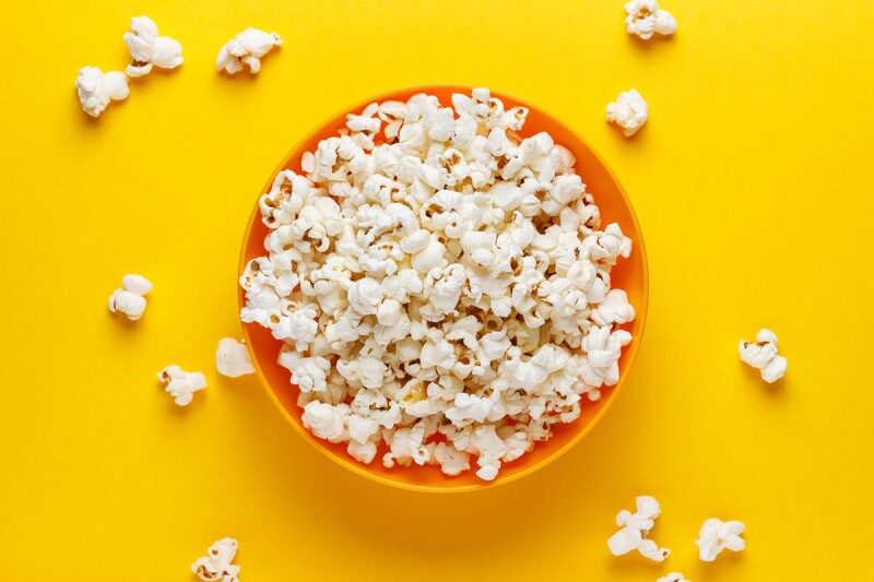 Top view of popcorn in an orange bowl on a yellow background. Popcorn is a great food to snack on late at night. 