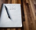 A notebook with sits on a table, with a pen resting on the page. There is a bulleted list on the paper with New Year's resolutions, including one to get better sleep in 2022.