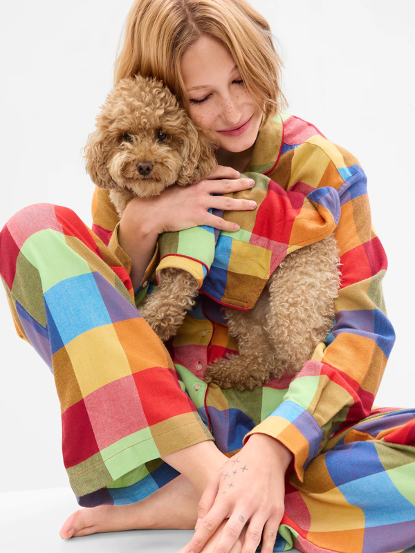 A woman in colorful plaid pajamas snuggling a dog in matching pjs.