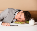 Boy falls asleep on a sandwich. He is tired and has put his head on the sandwich. He played too much with his phone and fell asleep.