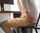 Person clutching their hip while sitting at a work desk