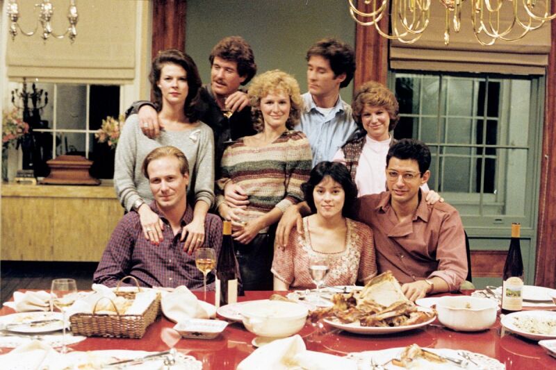 The cast of The Big Chill poses for a photo in front of a half-eaten Thanksgiving meal.