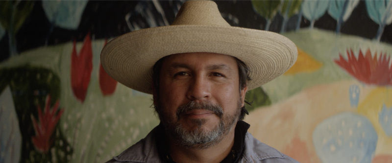 Texas artist Cruz Ortiz standing in front of one of his paintings.