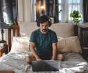 Man in green shirt listening to audio through headphones while sitting on his bed