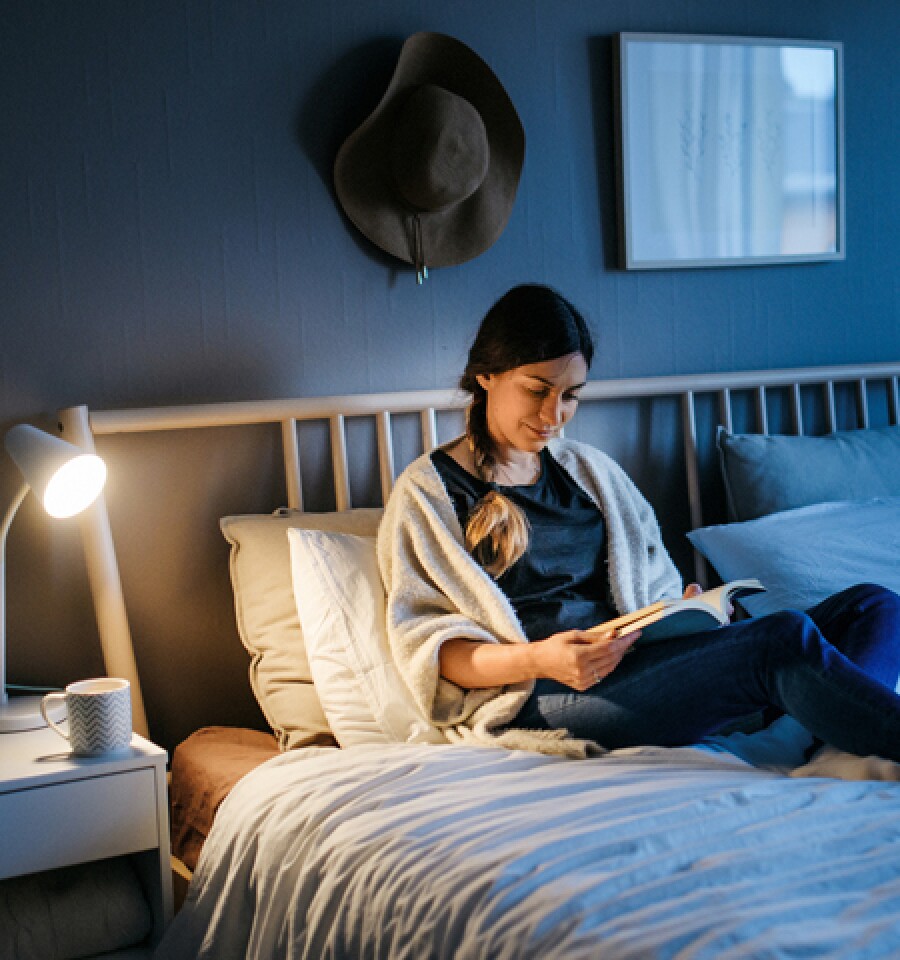 Woman reading paperback book at night with a bedside lamp