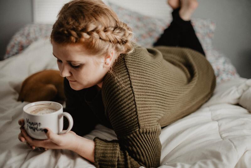 Woman drinking coffee out of a mug in bed.