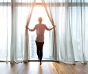 Woman opening curtains and looking out to a bright day