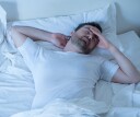 Man shifting in his bed, tossing and turning at night