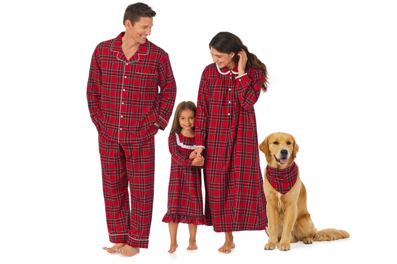 A mother, father, child, and dog pose for a photo while wearing matching, nostalgic Christmas pajamas.