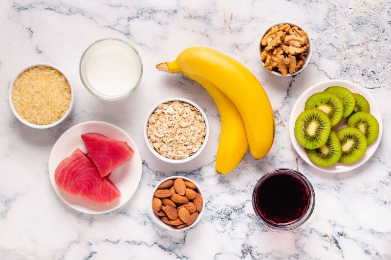 Different sized bowls of brown rice, oats, almonds, kiwi, and other foods that help you sleep through the night.