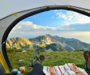 Two people sitting inside a tent enjoying a view of some mountains. The people are behind the view of the camera, with only their feet in the frame.