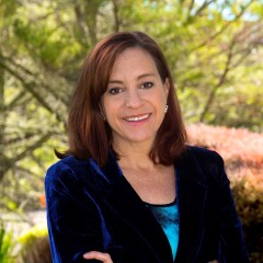 Writer and therapist Joanell Serra. She is standing outside with her arms crossed and smiling.