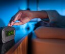 Woman pressing snooze button on early morning digital alarm clock.