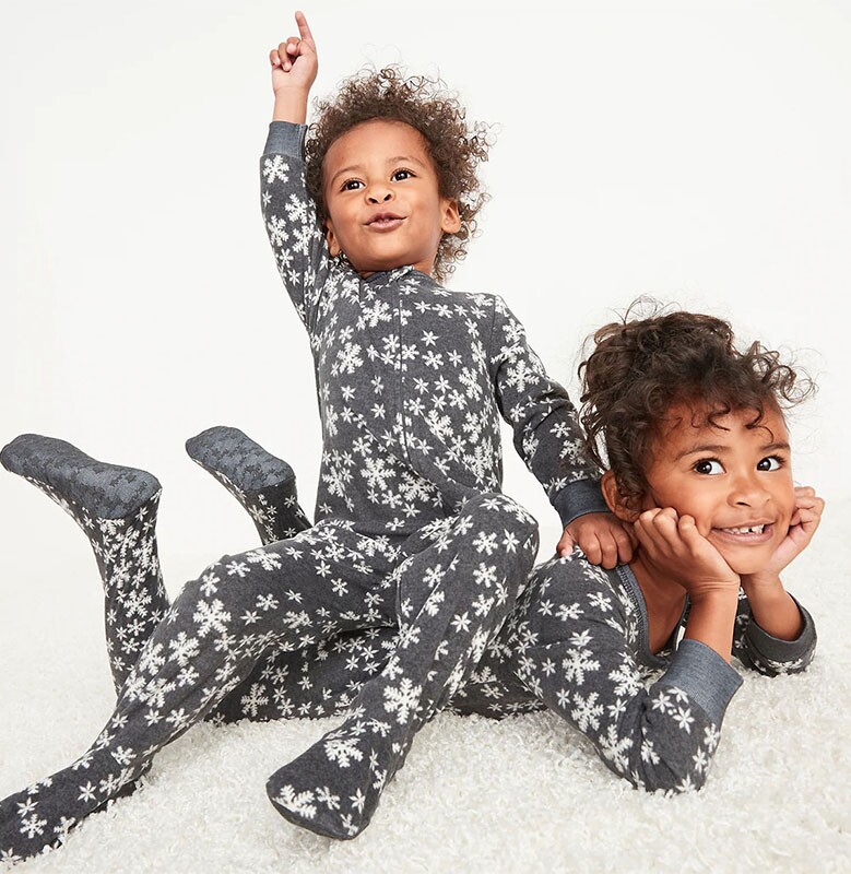 A young boy sitting on a slightly older girl's back in their matching family Christmas pajamas.