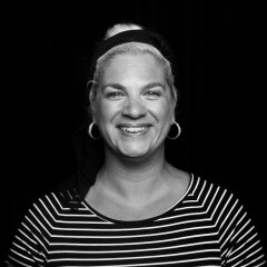 Black and white headshot of writer Jolie Kerr against a black background. She's smiling and wearing a striped shirt.