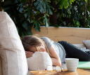 A woman laying on a cream couch taking a nap. Her glasses lay on a side table next to her.