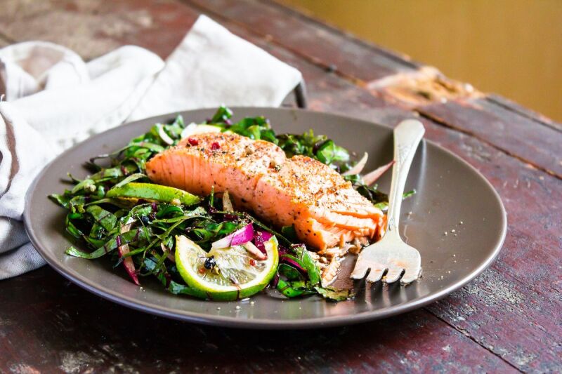 Cooked and seasoned fish on a bed of greens with lime garnish. Components of the Mediterranean diet and foods to help sleep.