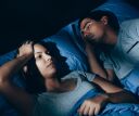 Woman trying to clam anxiety at night while her partner sleeps beside her.