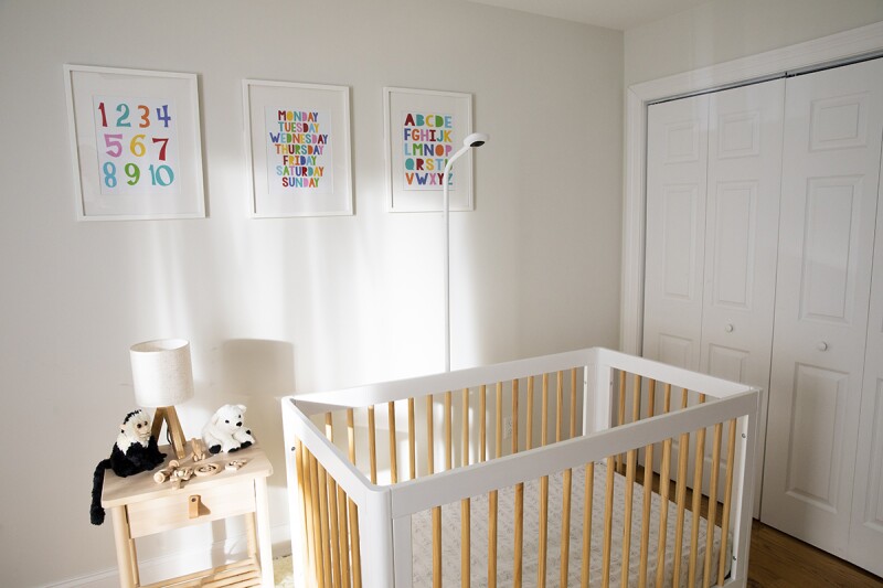 A furnished baby room with crib, nightstand, lamp, stuffed animals, numbers, letters, and a Nanit Pro floor stand. Check out our review of the Nanit by a mother who tried it.