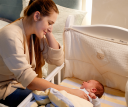 A woman looking over her baby in their crib.