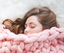 Person with long blonde hair snuggled up in a knitted peach blanket