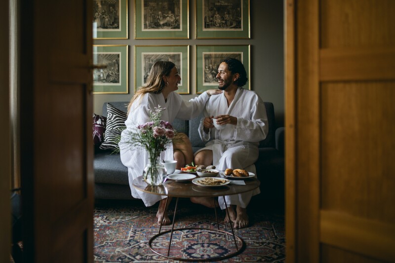 Happy couple in bathrobes, sitting in a fancy hotel, enjoying room service on their vacation