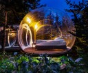 A bed sits in a plastic bubble, surrounded by an idyllic view of nature under moonlight. The Buubble Hotel in Iceland's Golden Circle is one of the coolest hotel beds in the world.