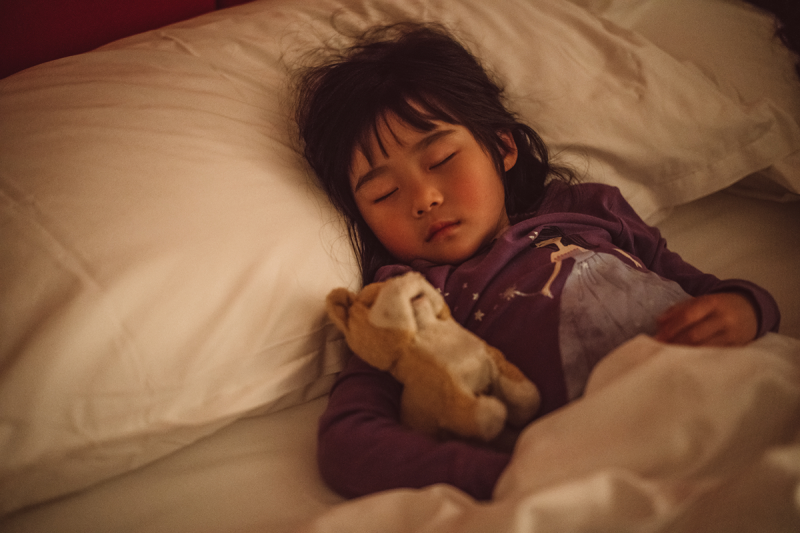 Little girl holding a toy sleeping soundly on the bed