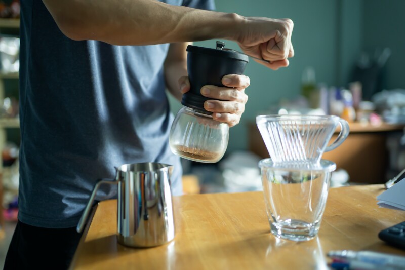 Person grinding coffee beans with a coffee grinder to make morning coffee and wake up