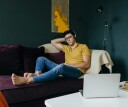 Attractive caucasian man sitting with eyes closed on the couch while having a nap listening music on headphones at home