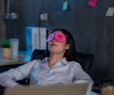 A woman leaning back with post-it notes over her eyes. The post-it notes have yes drawn on them.