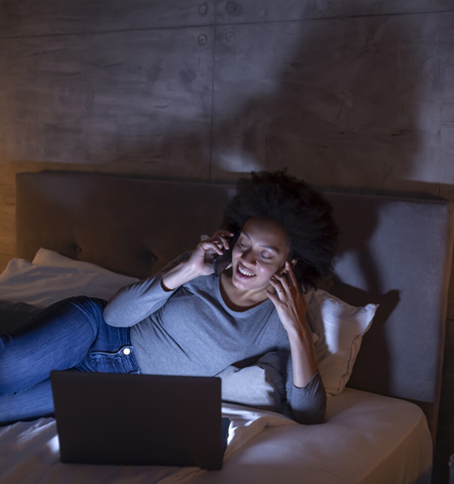 Person using phone and laptop in bed, in need of a digital detox and break