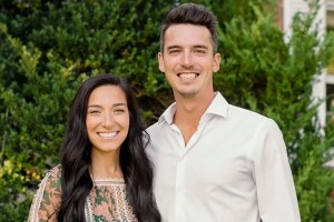 Jamie and Fillip Hord, the professional home and bedroom organizers behind Horderly, pose in front of green shrubbery.