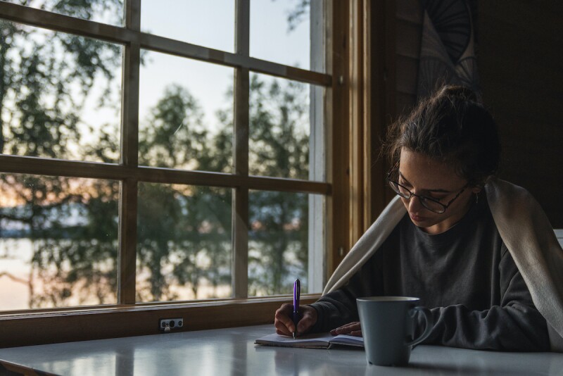 Woman journaling her dreams by a window as the sun rises